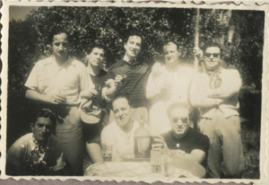 Archival black-and-white photograph of a group of people gathered outdoors around a table via Archivo de la Memoria Trans