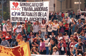 A large group of demonstrators gathers in a public square behind a banner reading "Union of Sex Workers of the Argentine Republic" held by the Asociación de Mujeres Meretrices de Argentina (AMMAR), a sex workers' rights organization. Source: AMMAR via Redtrasex