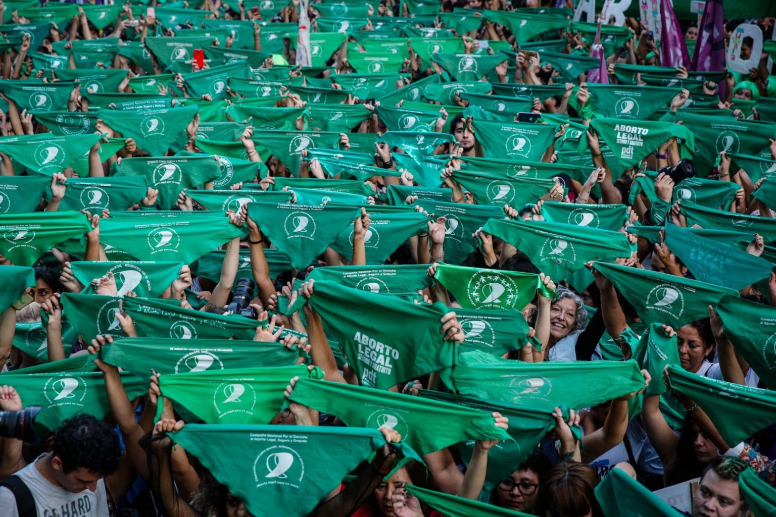 Color photograph of large crowd of people gathered during an Argentine Green Tide (Marea Verde) demonstration, raising the movement's iconic green bandanas in support of abortion rights.